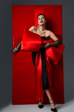 Mutlu Kadın 8 Mart 'ta Kırmızı Hediye alıyor. Büyük Kırmızı Fiyonklu Zarif Kadın ve İpek Kurdeleli Hediye Kutusu. Kokteyl Siyah Elbiseli Güzel Gülümseyen Kız kutluyor. Uluslararası Kadınlar Günü