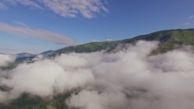 Sis ve sis dağların etrafında döner. Etrafta dönen alçak bulutların hızlandırılmış videosu. Yazın yeşil tepelerin arasında manzara sisli bir sabah. Resmedilmeye değer doğal manzara. Arka planda turist oteli olan manzara.