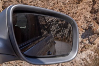 view on road and rocks in wind mirror of car going by dangerous road 