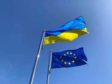 Ukrayna ve Avrupa Birliği bayrakları mavi gökyüzüne karşı bayrak direğinde