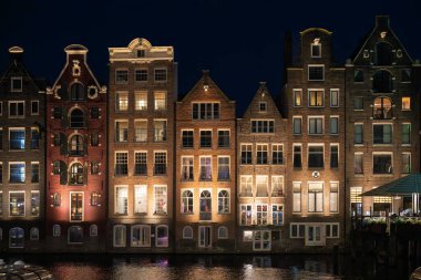 Hollanda, Amsterdam 'da geceleri sulara yansıyan bir dizi aydınlık kanal evi..