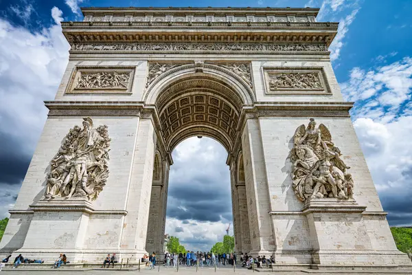 Paris 'teki Zafer Takı' nın detaylı bir perspektifi. Karmaşık oymalarını ve anıtsal mimarisini parçalı bulutlu gökyüzünün arka planına karşı sergiliyor..