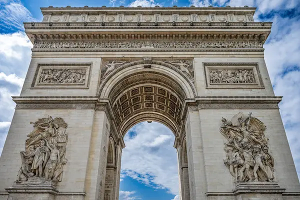 Paris 'teki Zafer Takı' nın detaylı bir perspektifi. Karmaşık oymalarını ve anıtsal mimarisini parçalı bulutlu gökyüzünün arka planına karşı sergiliyor..