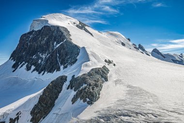 Dağcıların açık bir günde zirveye tırmandığı karla kaplı bir dağın çarpıcı manzarası..