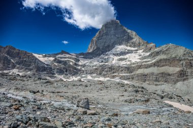 Buzulları olan Matterhorn dağı ve bulutlu mavi gökyüzünün altındaki kayalık bir arazide akan bir dere..