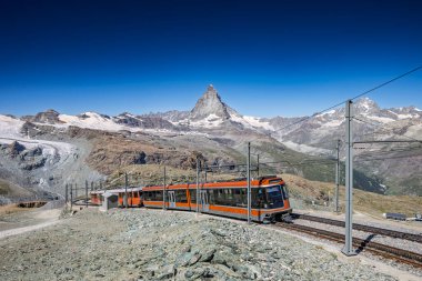 A train ascends through the Swiss Alps, showcasing the iconic Matterhorn peak in the background.