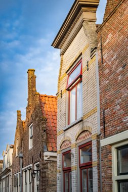 Hollanda 'nın Enkhuizen şehrinde, parlak mavi gökyüzü altında, tuğla cepheli, gablı çatıları ve kırmızı çerçeveli, büyüleyici bir sıra geleneksel Hollanda evi..