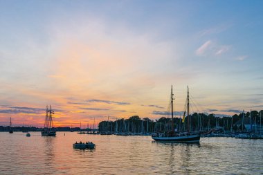 Almanya, Rostock 'taki Hanse Yelkenlisi sırasında gün batımında Warnow nehrinde yelken açan gemiler..