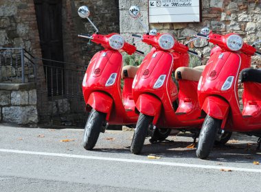CHIANTI, İtalya - 21 Eylül 2009: 3 adet parlak kırmızı Vespa scooterı. Vespa markası Enrico Piaggio tarafından 1946 yılında Roma 'da piyasaya sürüldü ve o zamandan beri özellikle şehir ortamında çok popüler bir ulaşım aracıdır.
