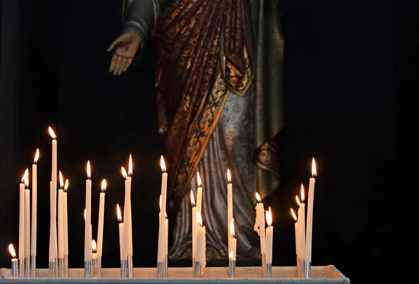 信者から教会で白い献身のろうそくを燃焼し 手と華やかなローブにスティグマとイエスの宗教彫刻の前で祈りと助けを求める — ストック写真