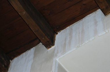 Su sızıyor ve koyu kahverengi ahşap kiriş tavanının altındaki alçılı iç duvarda ciddi su hasarına neden oluyor.