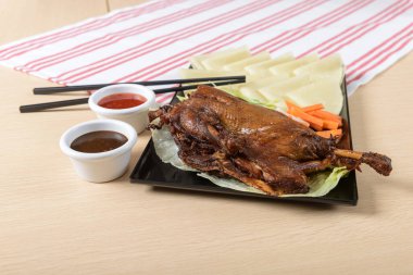 Kızarmış ördek, çıtır çıtır, siyah bir tabakta soslu, çubuklu ve garnitürlü.