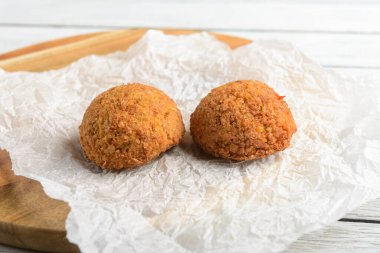 Kağıt tabakta iki falafel. Çörekler altın kahverengidir ve taze yapılmış gibi görünüyor. Kağıt tabak ahşap bir kesme tahtasına konur.