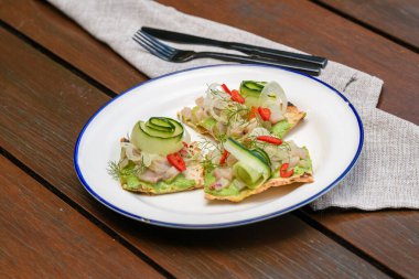 Üstünde Queensland kralbalığı, avokado sosu, salatalık kurdelesi, acı biber dilimleri ve dereotlu garnitür olan gevrek bir ekmek.