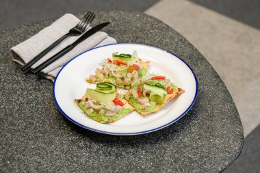 Üstünde Queensland kralbalığı, avokado sosu, salatalık kurdelesi, acı biber dilimleri ve dereotlu garnitür olan gevrek bir ekmek.