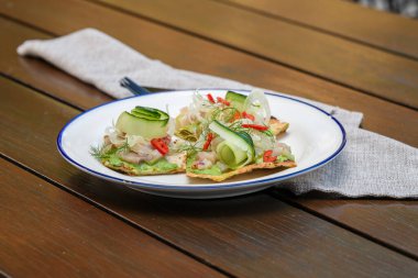 Üstünde Queensland kralbalığı, avokado sosu, salatalık kurdelesi, acı biber dilimleri ve dereotlu garnitür olan gevrek bir ekmek.