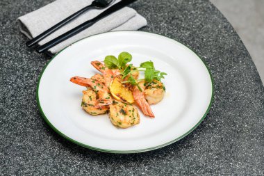 Taze otlar ve limon dilimleriyle süslenmiş ızgara Mooloolaba karidesleri.