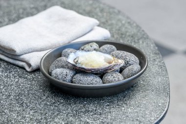 Taze istiridye, buzlu ve limonlu granitle süslenmiş siyah bir kasede soğuk taşlardan oluşan bir yatakta servis edilir.