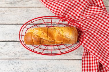 Taze pişmiş ekmek davetkar bir şekilde parlak kırmızı bir sepetin içinde, eskimiş ahşap bir masa üzerinde neşeli bir kareli kumaş eşliğinde, sıcak, sıcak bir atmosferi çağrıştırıyor paylaşmak için mükemmel.