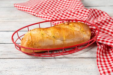 Sıcak bir somun altın ekmek canlı kırmızı bir sepet içinde, kırsal bir kareli kumaşla çevrili. Yumuşak ışık davetkar dokuları vurgular, rahatlatıcı bir yemek için mükemmeldir..
