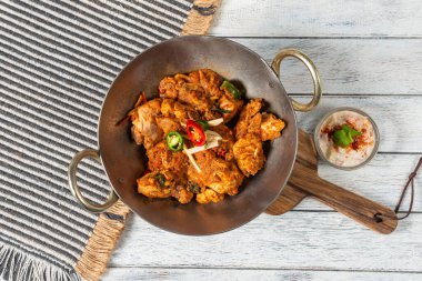 Canlı bir tabak baharatlı tavuk taze otlar ve biberlerle süslenir, ahşap bir tahtanın üzerinde, küçük bir bardak soğutucu yoğurt sosunun yanında, sıcaklık ve lezzeti çağrıştırır..