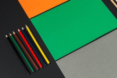 Turuncu, yeşil ve gri renkli renkli kağıtlar sanatsal keşifleri bekliyor. Yanlarında renkli kalem ve fırça koleksiyonu var. Yaratıcılık ve hayal gücünü ateşliyor..