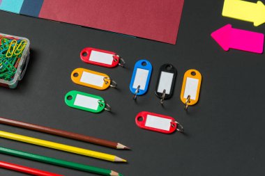 A colorful arrangement of various stationery items features labels in bright hues, paper clips, pencils, and colored sheets spread across a dark surface, highlighting creativity and organization.