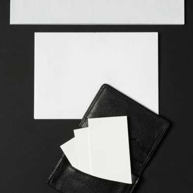 Parlak siyah bir cüzdan açık duruyor, içinde boş kartlar var. Yukarıda, beyaz bir zarf, yaratıcılığı davet eden minimalist bir estetik yaratarak, karanlık zemin ile çelişiyor..