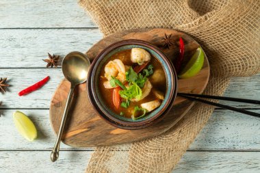 Baharatlı deniz ürünleri çorbası ahşap bir tabakta güzel bir şekilde duruyor. Bitkiler ve limon dilimleriyle süslenmiş. Mutfak lezzeti ve sıcaklığın özünü yakalıyor..