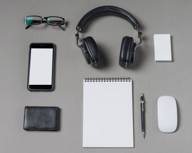 İyi düzenlenmiş bir çalışma alanı kulaklıklar, gözlükler, şık bir telefon, bir defter, bir kalem ve şık bir cüzdan içerir. Her öge pürüzsüz gri bir yüzeye düzgün bir şekilde yerleştirilmiştir..