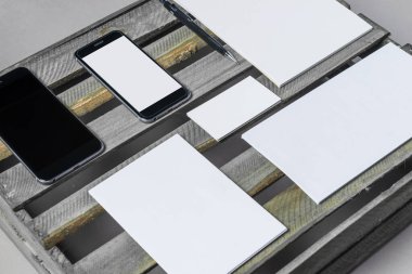 Kırsal yeşil ahşap bir yüzeye yerleştirilmiş boş kırtasiye ve mobil cihazlar koleksiyonu, güneşli bir öğleden sonra tasarım çalışmalarında ilham ve yaratıcılığı teşvik eder..