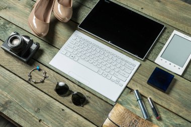 Şık bir çalışma alanında, şık ayakkabılar ve güneş gözlükleriyle çevrili bir kamera, dizüstü bilgisayar ve e-okuyucu sergilenir. Ahşap yüzey, bu modern yaratıcılığa kırsal bir cazibe katıyor..