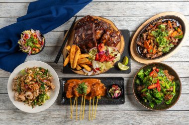 Izgara etler, taze salatalar ve aromalı soslar içeren canlı bir tabak çeşidi masayı doldurur. Kırsal ahşap arka plan, gün batımında bu davetkar yemek deneyimine sıcaklık katıyor..