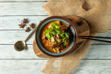Taze kişniş ile çevrili taze etle dolu lezzetli bir güveç kasesi. Bu ağız sulandırma kabı, cezbedici cazibesini artırmak için ahşap bir yüzeyin üzerinde oturur..