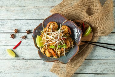İçinde karides, fasulye filizi ve limon dilimleri olan rengarenk kızarmış şehriyeler çok cazip bir yemek yaratıyor. Kırsal ahşap arka plan çekicilik katar, bu lezzetli yemeğin tadını çıkarmaları için lokantaları davet eder.