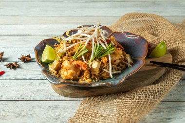 Canlı bir tabak kızarmış şehriye taze otlar, limon kamaları ve fasulye filizleri ile süslenmiş köy ahşabı bir masada duruyor. Günbatımının ılık tonları davetkar bir atmosfer yaratır..