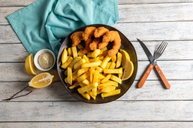 Cömert bir porsiyon altın kızartma ve kıtır kıtır lezzet, kara bir tabakta duruyor. Taze limon dilimleri ve küçük bir tabak tartar sosu bu ağız sulandıran sunuma lezzet katar..