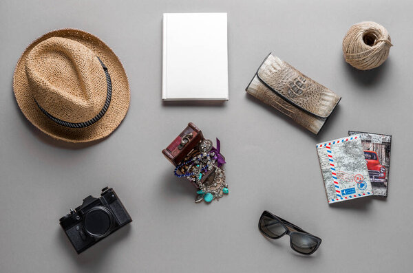 A collection of travel essentials lies beautifully arranged on a smooth surface. A camera, journal, sunglasses, and a straw hat evoke a spirit of creativity and exploration under soft lighting.