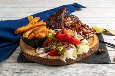 Çok güzel hazırlanmış bir tabakta leziz barbekü kaburgaları, çıtır çıtır patates kızartmaları ve taze sebzelerle dolu limonla süslenmiş canlı bir salata var. Lezzetli bir dokunuş için mükemmel, her yemek için mükemmel..