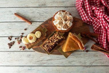 A beautifully arranged assortment of desserts features a creamy cake topped with swirls, flaky pastries, and a slice of rich pie. The rustic wooden board adds warmth to this delightful treat.