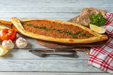 A beautifully presented flatbread, freshly baked, features a rich filling of minced meat and spices. Surrounded by fresh vegetables and lemon, it entices the senses with vibrant colors and flavors.