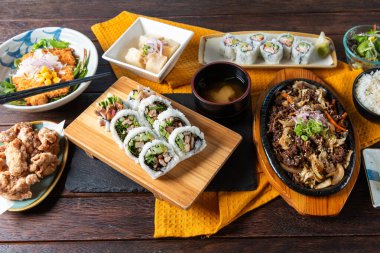 A mouthwatering display of sushi rolls, fried chicken, and garnish salad arranged artistically on a wooden table. The colors and textures create an inviting atmosphere for a culinary feast.