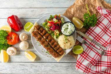 Platter features skewers of perfectly grilled meat accompanied by fluffy rice, fresh salad, and creamy yogurt. Brightly colored vegetables and lime slices enhance the vibrant presentation.