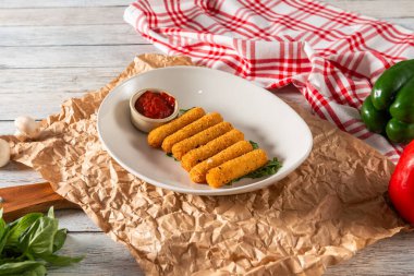 Bir tabak altın kızartma aperatifi, küçük bir kase keskin sosla birlikte buruşmuş kağıda güzelce konur. Taze sebzeler ve otlar rengarenk bir dokunuş katar..