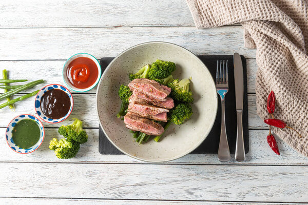 Tender slices of steak are elegantly arranged atop a bed of crisp broccoli. Accompanied by a variety of sauces, this culinary creation invites taste and creativity.