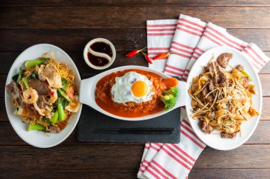 Üç canlı yemek kırsal bir ahşap masada güzelce düzenlenmiştir. Orta kısımda, rengarenk kızarmış şehriye ve sebzelerle çevrili doyurucu bir yumurta tepeli yemek ve lokantaları davet eden.