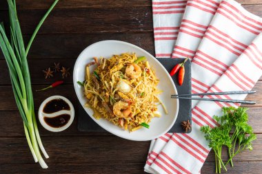 Lezzetli bir karides ve erişte karışımı ince siyah bir tabakta ustalıkla düzenlenir. Aromatik otlar ve baharatlar yemeğin etrafını sarmış. Mutfak zevkini çağrıştırıyor..