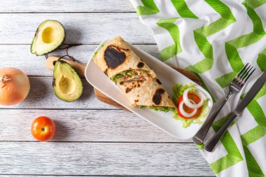 Taze sebzelerle dolu canlı bir paket ve kremalı avokado şık bir tabakta duruyor. Yanında dilimlenmiş soğan, yarım avokado ve turunçgiller kırsal masa düzenine renk katar..