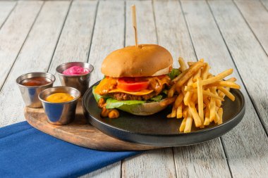 Ağız sulandıran bir burger taze sebzelerle ve erimiş peynirle dolu ahşap bir tabakta duruyor. Kızarmış patatesler ve renkli soslarla birlikte bu yemek hoşgörüyü davet ediyor..