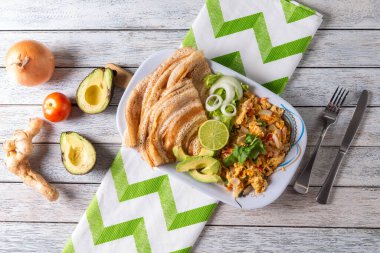 Renkli bir tabakta kabarık yumurta, çıtır ekmek, taze avokado dilimleri ve canlı garnitürler yer alıyor. Bu nefis brunch, dokulu bir masada, davetkar bir lezzet ve sıcaklıkla hazırlanmıştır..